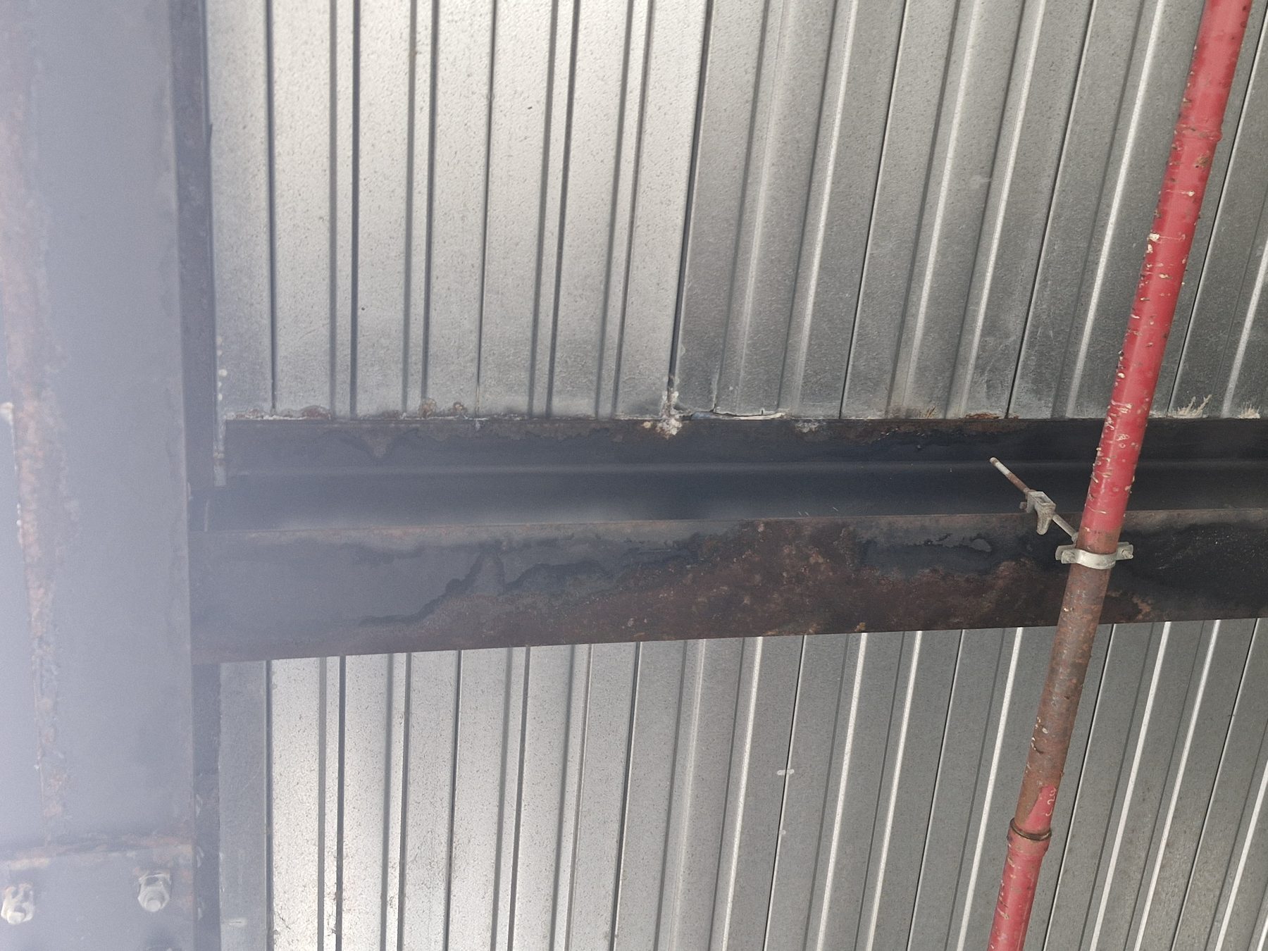 Corroded structural steel beam beneath roof sheeting